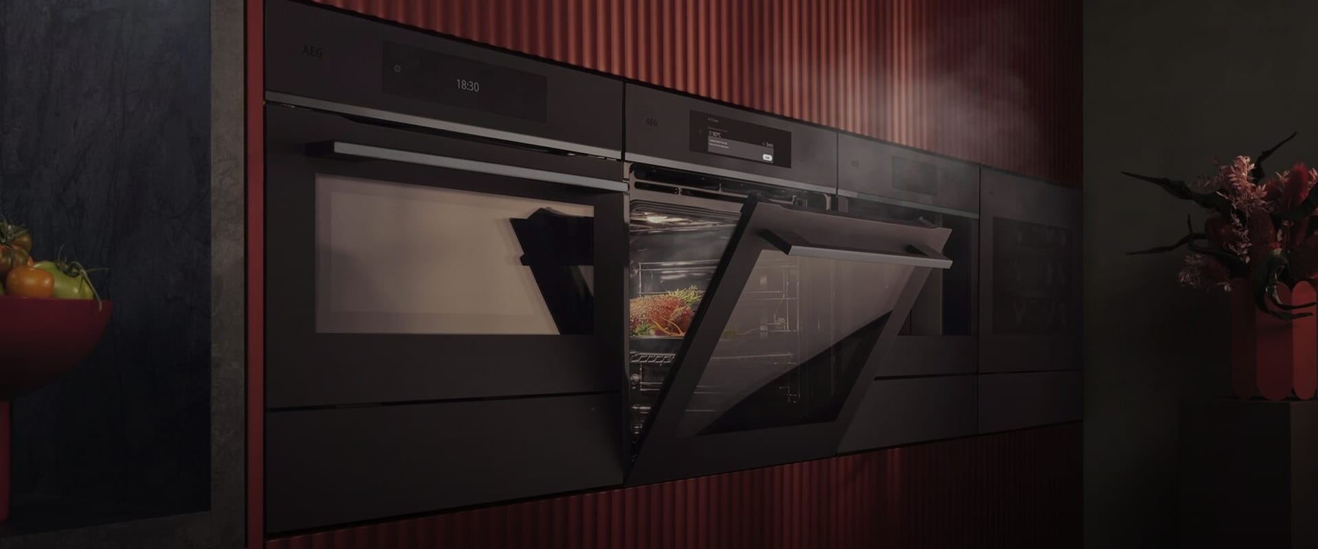 En innebygd AEG-dampovn i en moderne kjøkkenvegg med røde, riflede paneler som viser matlaging med damp